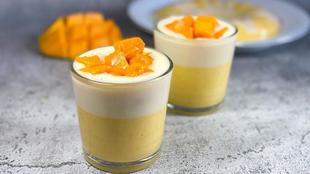 Puding mangga keju lembut dengan lapisan warna cerah, dihias daun mint untuk sentuhan elegan